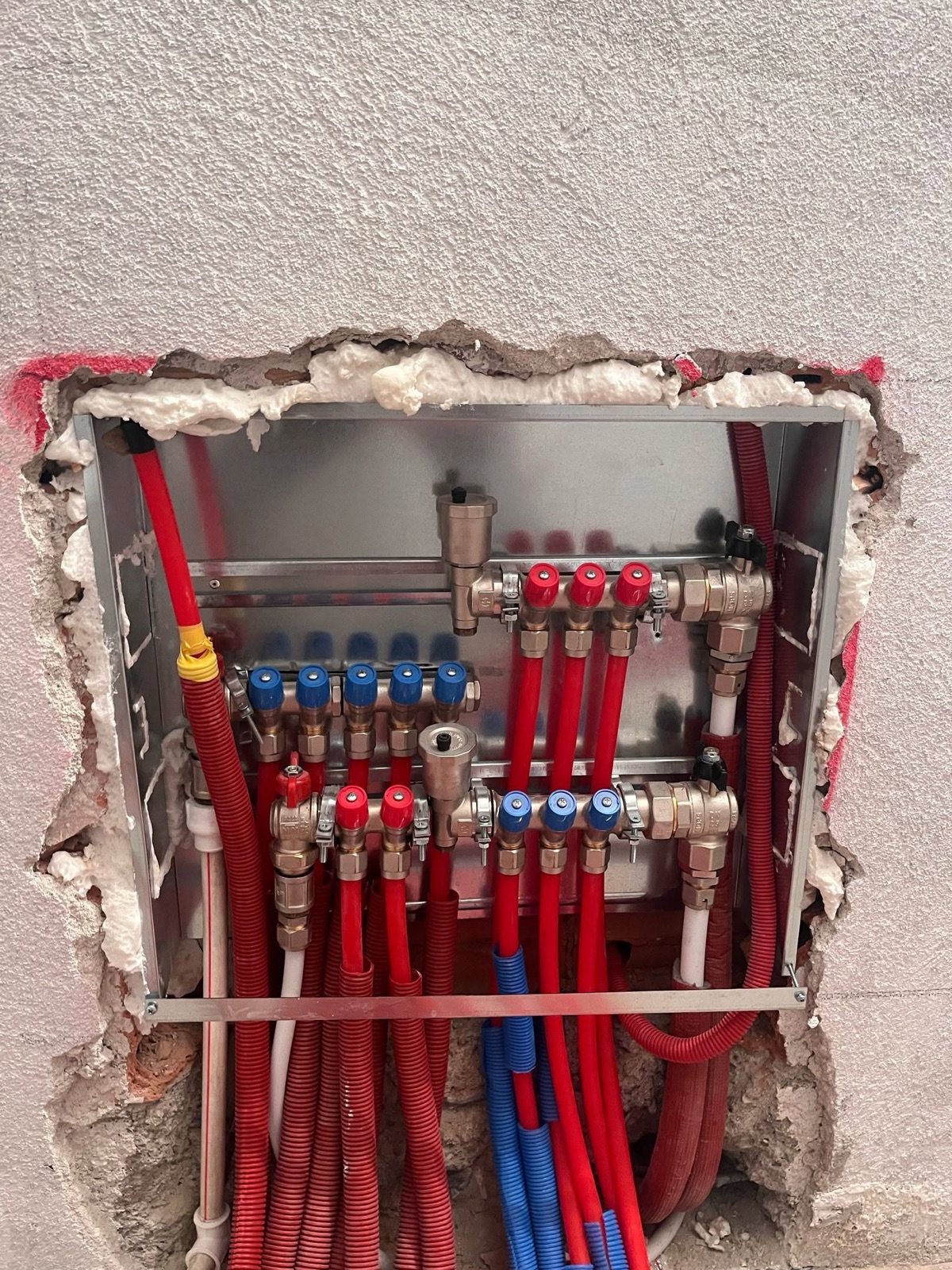 Kolektor me tubacione të kuqe e blu gjatë instalimit të ngrohjes