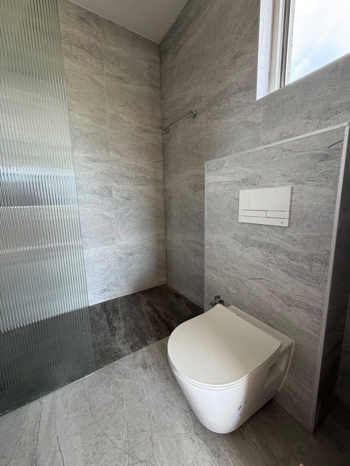 WC e bardhë në banjo me pllaka gri dhe ndarje prej xhami